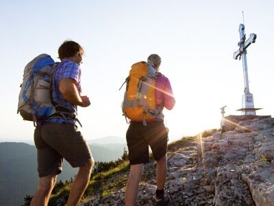 Zwei Wanderer stehen bei Sonnenaufgang am Gipfelkreuz des Wallberg am Tegernsee 