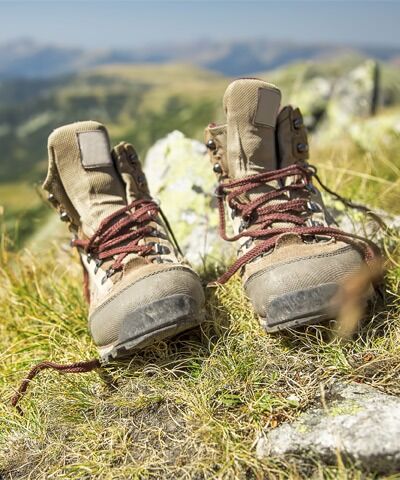 Ein paar alte Bergschuhe mit roten Schnuersenkeln stehen geoeefnet alleine auf Gras und Steine 