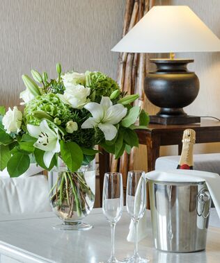 Blick in das Wohnzimmer der Senior Suite Hotel Der Westerhof Tegernsee auf dem Couctisch steht ein eleganter Blumenstrauss ein Sektkuebel mit einer Flasche Champagner und zwei Glaeser