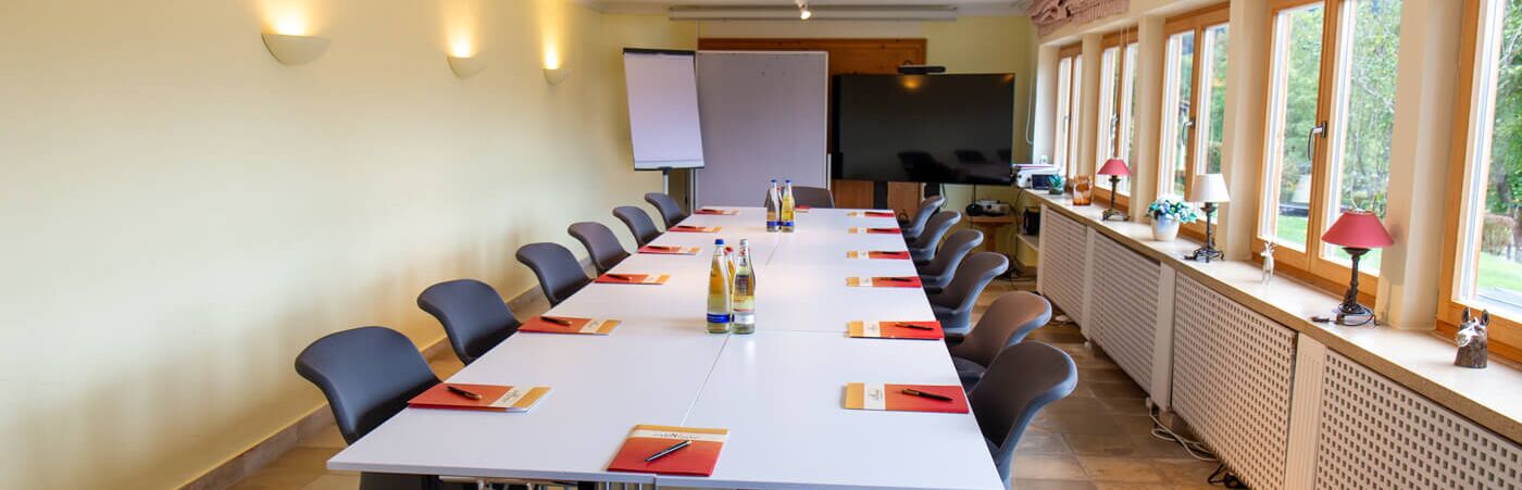 Conference room at Hotel Der Westerhof Tegernsee Stone tiled floor U-shaped seating Projector screen and flipchart in the background Four large windows Daylight with access to terrace with lake view