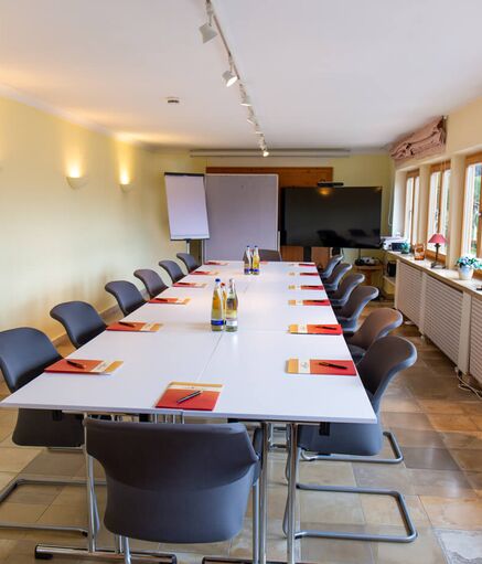 Conference room at Hotel Der Westerhof Tegernsee Stone tiled floor U-shaped seating Projector screen and flipchart in the background Four large windows Daylight with access to terrace with lake view