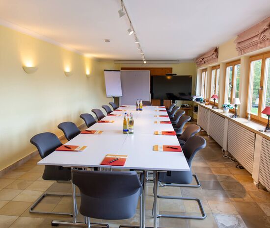 Tagungsraum im Hotel Der Westerhof Tegernsee Steinfliesenboden Bestuhlung in U-Form Beamer Leinwand und Flipchart im Hintergrund vier grosse Fenster Tageslicht mit Austritt auf Terrasse mit Seeblick 