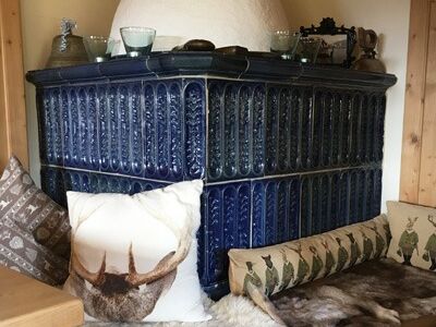 Alter Kachelofen mit blauen Kacheln im Hotel Der Westerhof und eine Eckbank mit Kissen und Lamm- und Hirschfellen als Sitzkissen