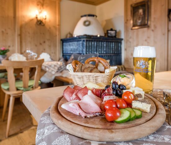 Snack board in the rustic Bauernstueberl in the Hotel Der Westerhof in the background original tiled stove with blue tiles